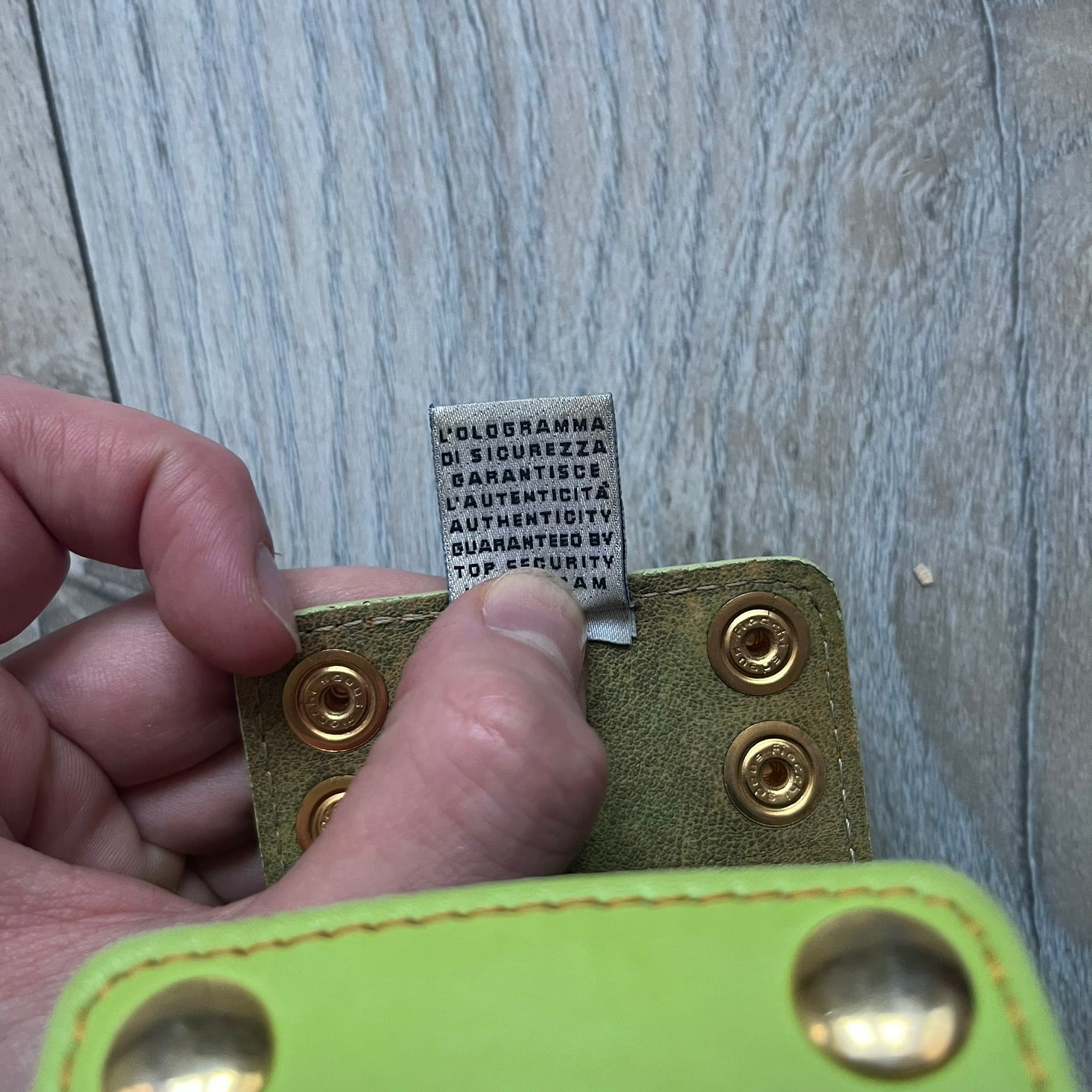 The Dolce &amp; Gabbana Big Green Leather Bracelet is a tall green leather wristband featuring a layered D&amp;G logo along its length - an orange base layer with a green logo on top, detailed with visible orange stitching. The inside has a Dolce &amp; Gabbana tag, and it closes with two metal buttons, offering four total button positions for adjustable sizing.