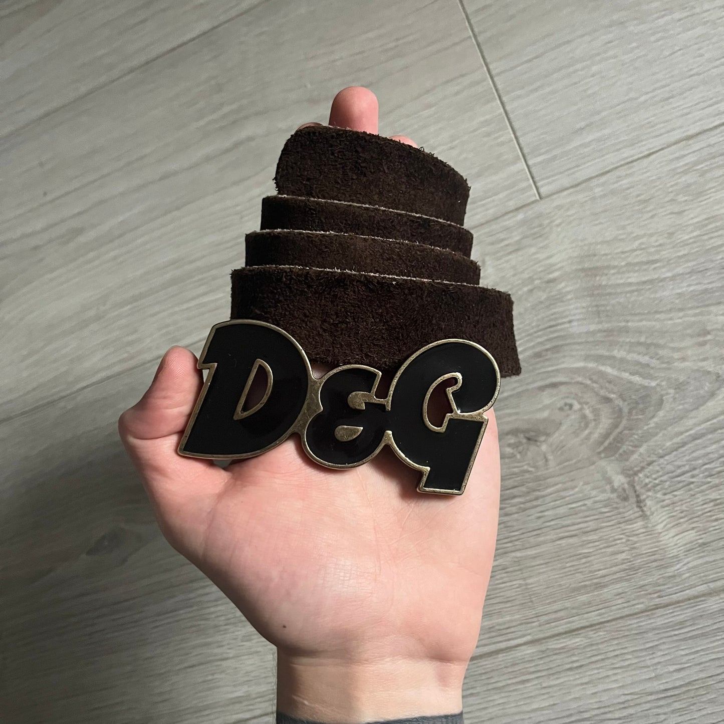 Dolce & Gabbana Black Enamel Belt featuring a D&G logo buckle in black enamel with gold-tone outline. Crafted from brown leather with a gold-tone interior, this belt combines sleek design with subtle luxury detailing.