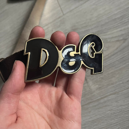 Dolce & Gabbana Black Enamel Belt featuring a D&G logo buckle in black enamel with gold-tone outline. Crafted from brown leather with a gold-tone interior, this belt combines sleek design with subtle luxury detailing.