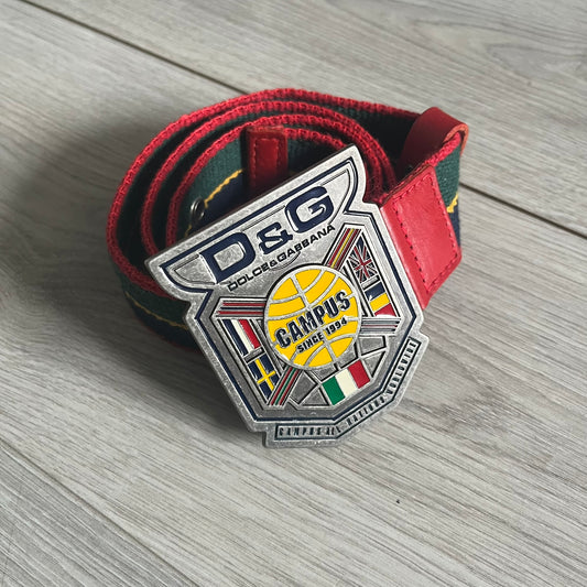 Dolce &amp; Gabbana "Campus Since 1994" Material Belt features a multicolor cotton webbing strap in red, navy, green, and yellow with leather-tipped ends. The statement metal buckle displays a crest design with D&amp;G branding, a central “Campus Since 1994” motif, and multiple national flags. A sporty accessory that combines vintage with luxury detail.
