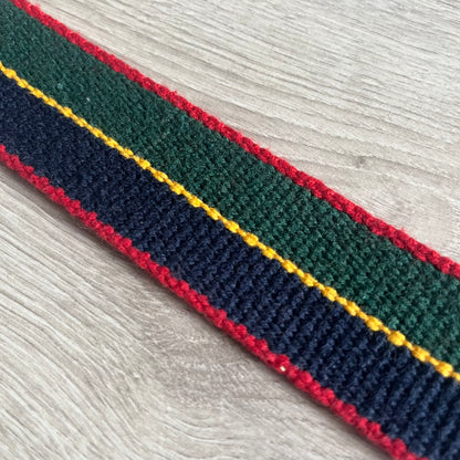 Dolce &amp; Gabbana "Campus Since 1994" Material Belt features a multicolor cotton webbing strap in red, navy, green, and yellow with leather-tipped ends. The statement metal buckle displays a crest design with D&amp;G branding, a central “Campus Since 1994” motif, and multiple national flags. A sporty accessory that combines vintage with luxury detail.