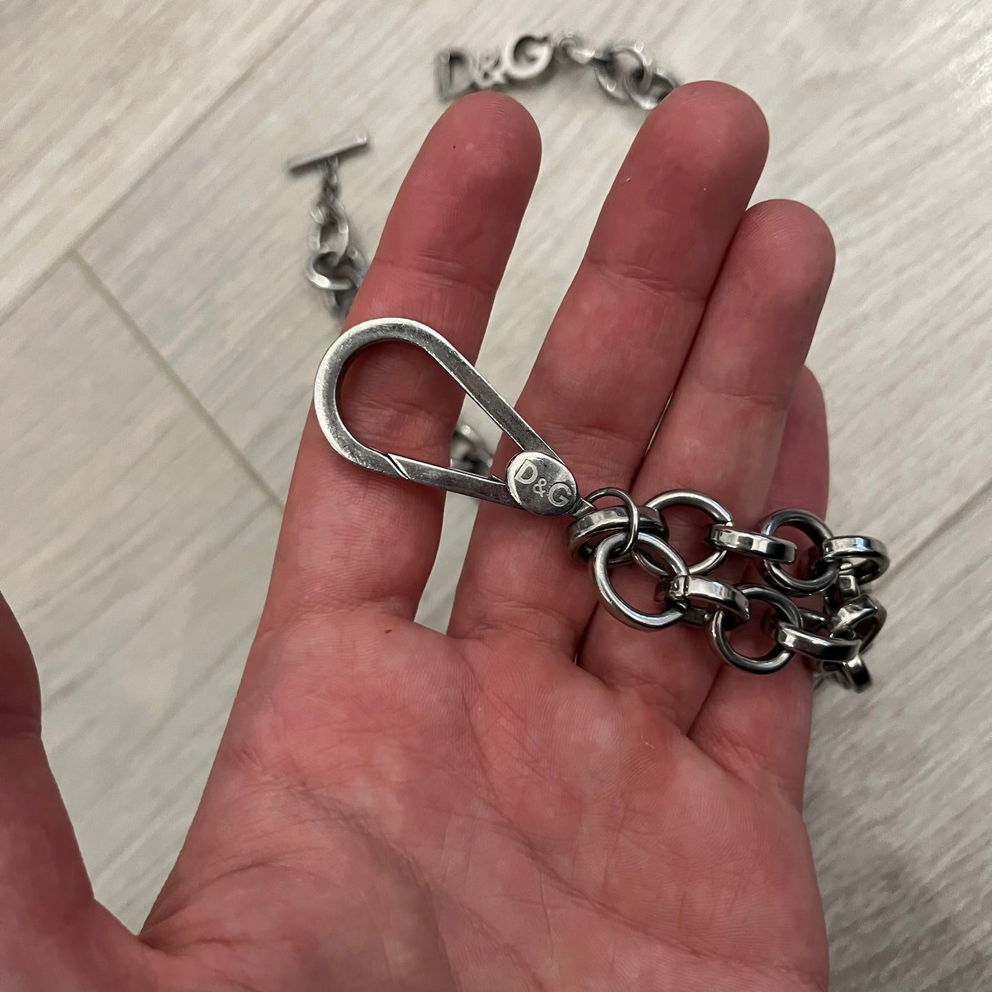 Dolce &amp; Gabbana Carabiner Chain Necklace features a robust stainless steel chain with a central carabiner engraved with the D&amp;G logo. The adjustable design includes a bolt-style clasp to modify the length, and the opposite end showcases a three-dimensional D&amp;G logo, blending industrial detailing with high-fashion appeal.