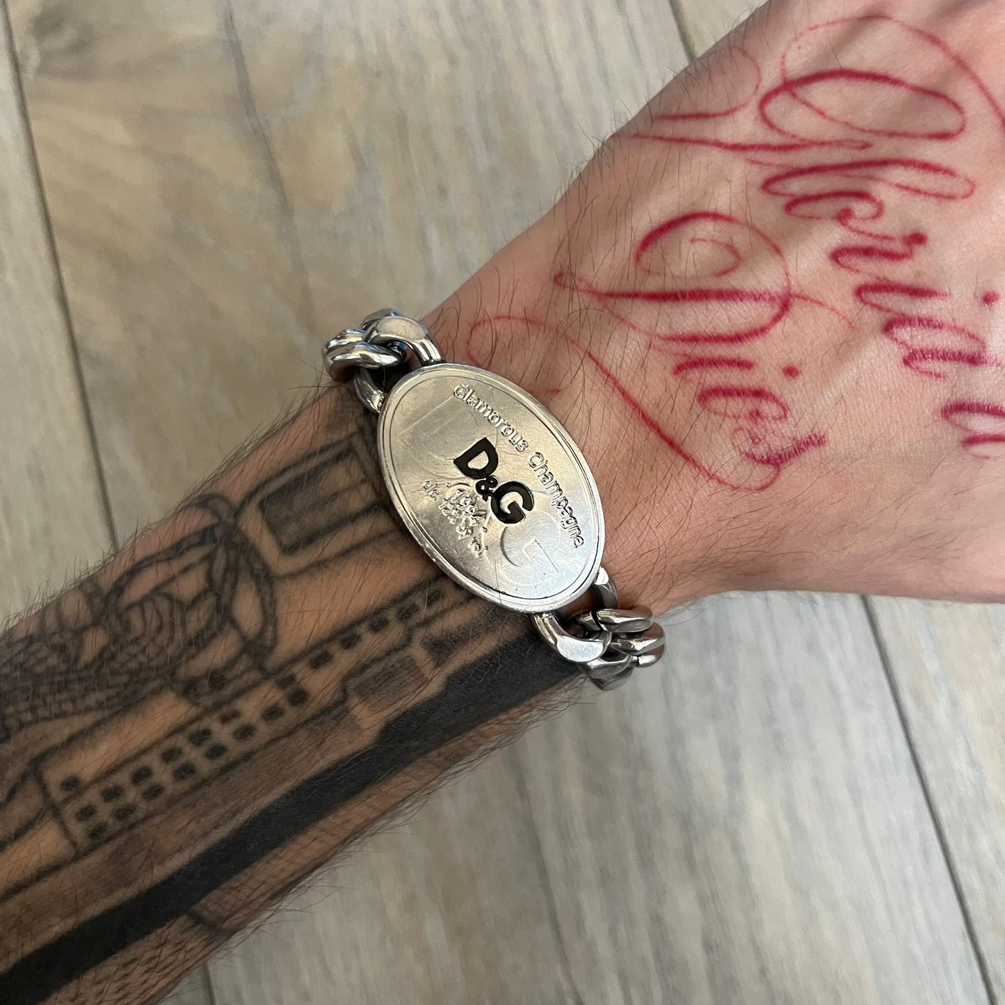 Dolce &amp; Gabbana Champagne Bracelet DJ1092 is a stainless steel bracelet. The silver-tone metal plate is shaped like a D&amp;G champagne label and displays a black D&amp;G logo, along with engraved “Glamorous Champagne 1994 Alc. 12% by Vol.” text. The back of the plate features a large, shallow engraved D&amp;G logo. Retailed at 125 usd in 2000's.
