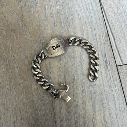 Dolce &amp; Gabbana Champagne Bracelet DJ1092 is a stainless steel bracelet. The silver-tone metal plate is shaped like a D&amp;G champagne label and displays a black D&amp;G logo, along with engraved “Glamorous Champagne 1994 Alc. 12% by Vol.” text. The back of the plate features a large, shallow engraved D&amp;G logo. Retailed at 125 usd in 2000's.