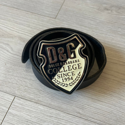 Dolce & Gabbana “College Since 1994” belt featuring a pretty big crest-shaped buckle. The silver text overlays a white-and-black split crest, paired with a soft black leather strap for a refined yet edgy finish.