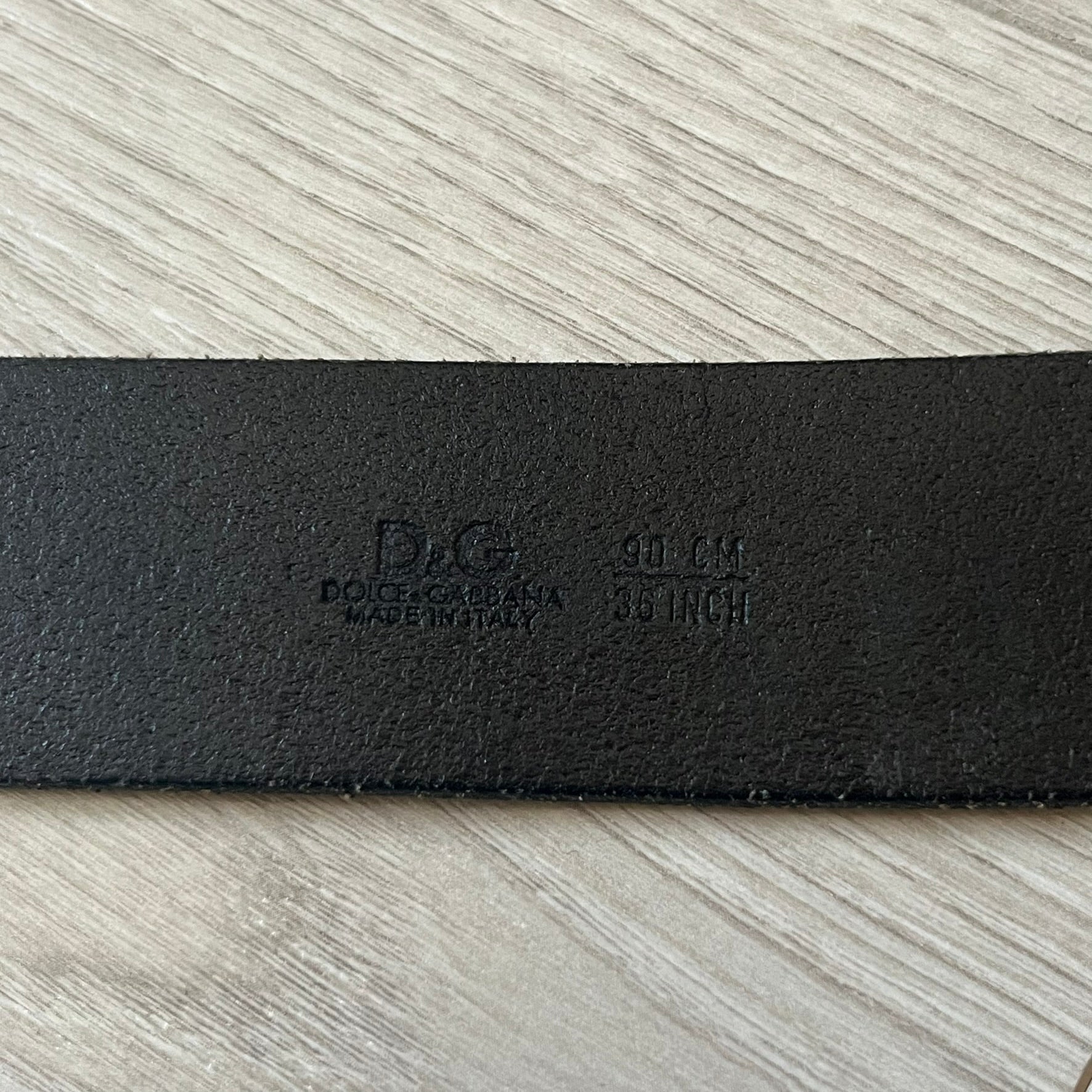  Dolce &amp; Gabbana “College Since 1994” belt featuring a pretty big crest-shaped buckle. The silver text overlays a white-and-black split crest, paired with a soft black leather strap for a refined yet edgy finish.