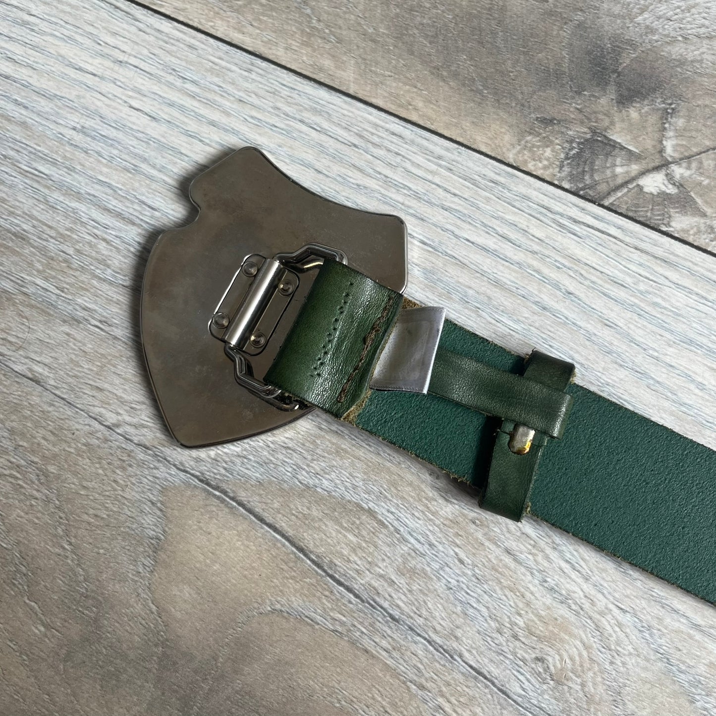 Dolce &amp; Gabbana “College Since 1994” belt featuring a big crest-shaped buckle. The silver text overlays a beige-and-black diagonally split crest, paired with a soft green leather strap in a washed style.