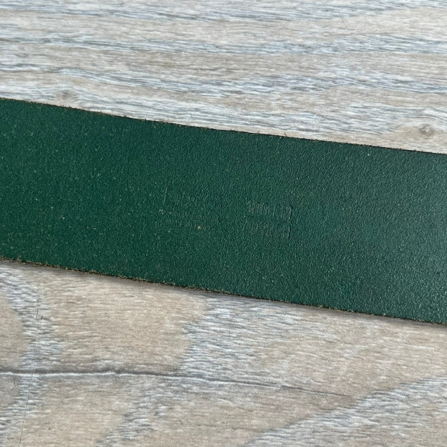 Dolce &amp; Gabbana “College Since 1994” belt featuring a big crest-shaped buckle. The silver text overlays a beige-and-black diagonally split crest, paired with a soft green leather strap in a washed style.