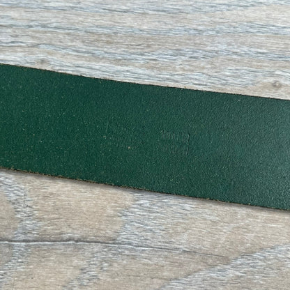 Dolce &amp; Gabbana “College Since 1994” belt featuring a big crest-shaped buckle. The silver text overlays a beige-and-black diagonally split crest, paired with a soft green leather strap in a washed style.