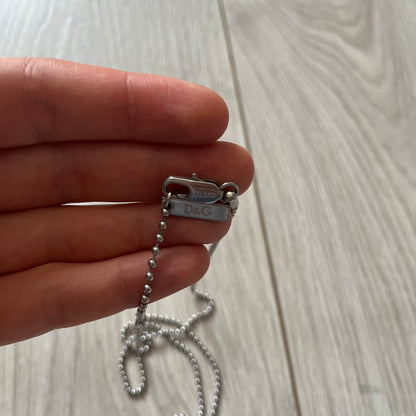Hand holding a silver chain with a D&G tag on a light wooden surface