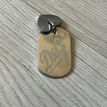 Gold dog tag with 'D&G' logo on a textured surface