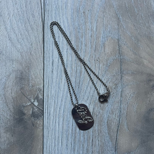 The Dolce & Gabbana Crystal Logo Dog Tag Necklace features a silver-tone ball chain with two pendants: a plain dog tag and a cutout D&G logo adorned with crystals. It has a large clasp engraved with D&G and model markings, from the 2000s.