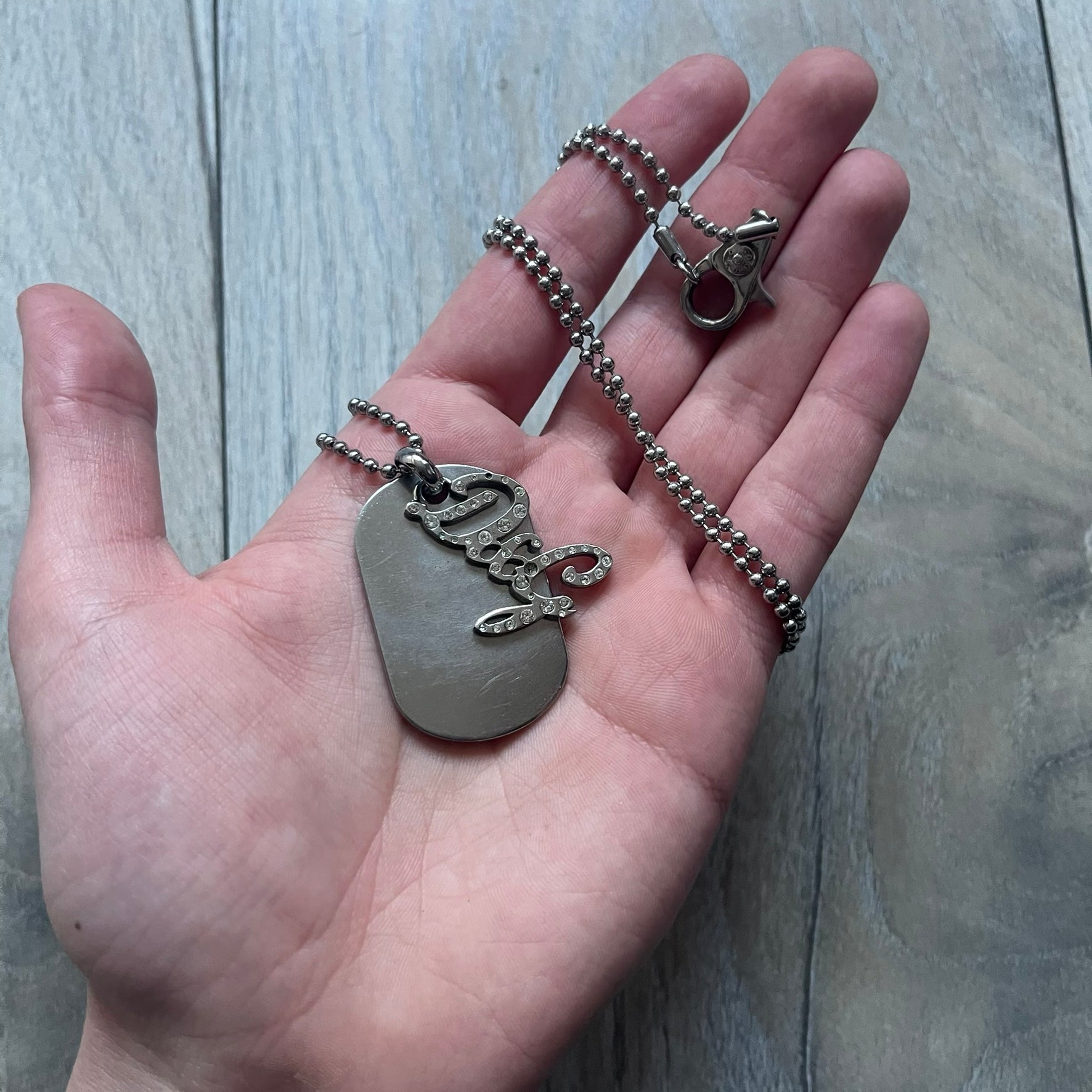 The Dolce & Gabbana Crystal Logo Dog Tag Necklace features a silver-tone ball chain with two pendants: a plain dog tag and a cutout D&G logo adorned with crystals. It has a large clasp engraved with D&G and model markings, from the 2000s.