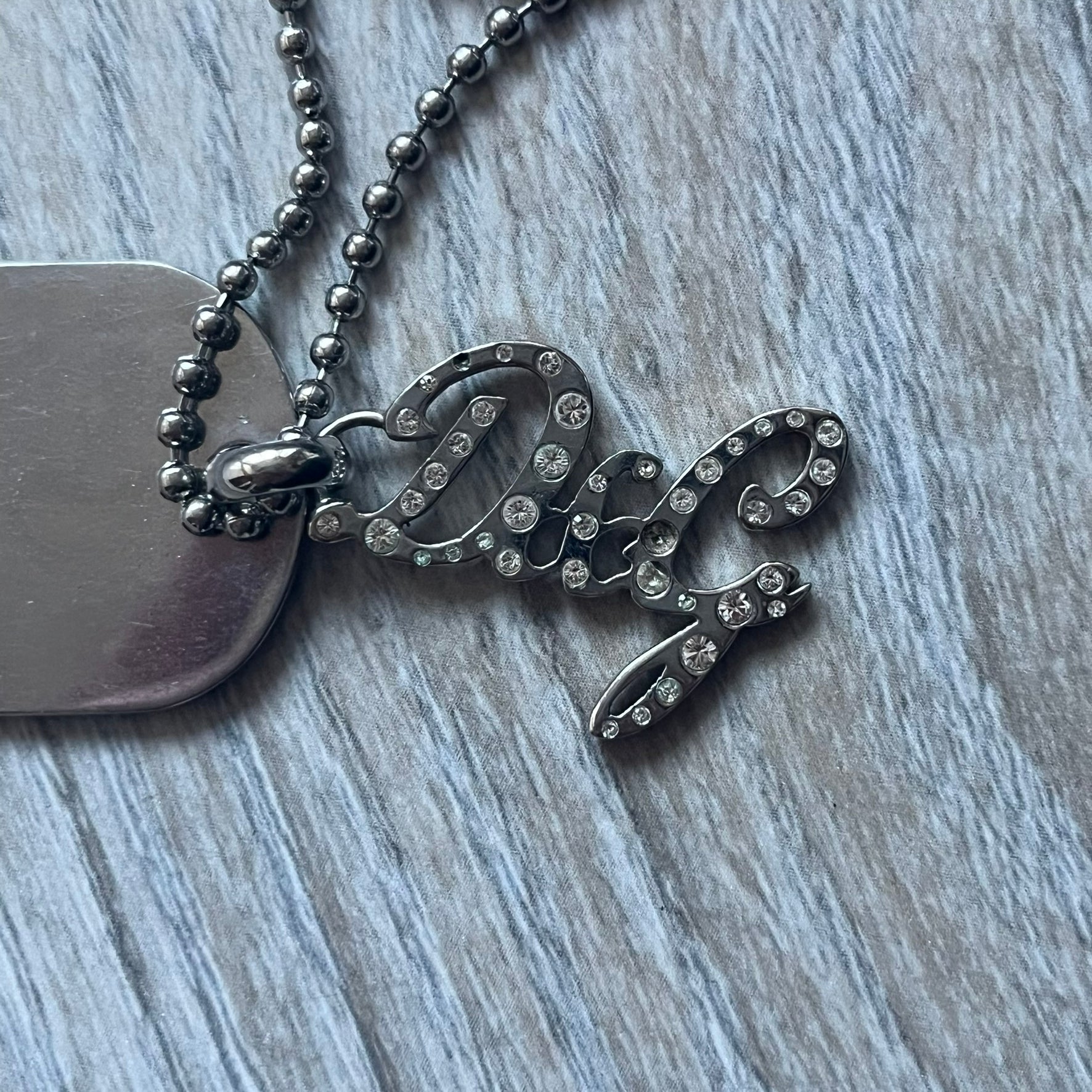 The Dolce & Gabbana Crystal Logo Dog Tag Necklace features a silver-tone ball chain with two pendants: a plain dog tag and a cutout D&G logo adorned with crystals. It has a large clasp engraved with D&G and model markings, from the 2000s.