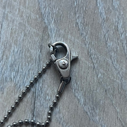 The Dolce & Gabbana Crystal Logo Dog Tag Necklace features a silver-tone ball chain with two pendants: a plain dog tag and a cutout D&G logo adorned with crystals. It has a large clasp engraved with D&G and model markings, from the 2000s.