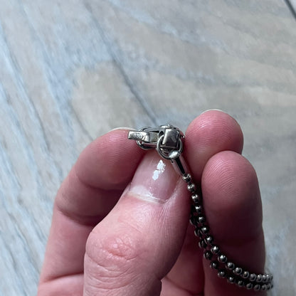 The Dolce & Gabbana Crystal Logo Dog Tag Necklace features a silver-tone ball chain with two pendants: a plain dog tag and a cutout D&G logo adorned with crystals. It has a large clasp engraved with D&G and model markings, from the 2000s.