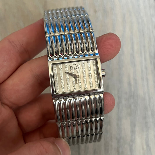 Dolce &amp; Gabbana Crystals Analog Watch is a stainless steel quartz watch featuring a square dial with fully crystal face, silver hands and small D&amp;G logo. The case and bracelet form a continuous design with the face matching the width of the bracelet. The bracelet is made from small silver rectangles. It includes a dual side-clasp closure, is water resistant to 3 ATM, with removable links. Comes with an extra link.