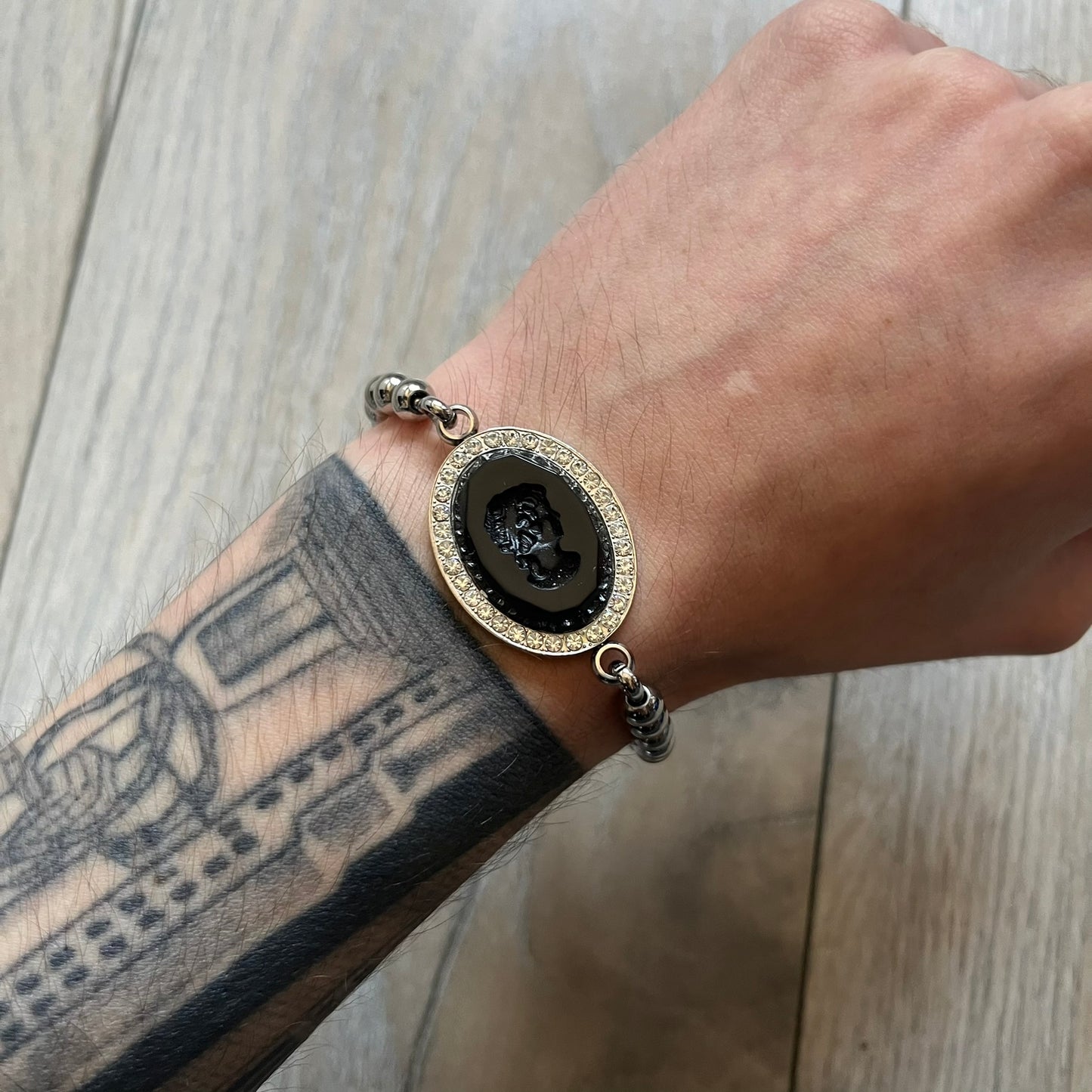 Dolce & Gabbana DJ0162 stainless steel bracelet designed as part of a three-bracelet watch set. Constructed with a bead-style chain and secured with a T-bar clasp, with D&G branding engraved on the T-bar and on the circular clasp ring. The centerpiece is an oval black stone engraved with a face design, framed by crystal embellishments.