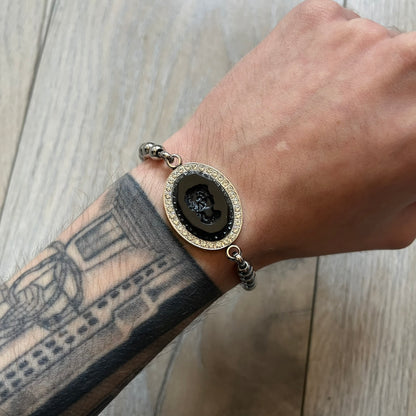 Dolce & Gabbana DJ0162 stainless steel bracelet designed as part of a three-bracelet watch set. Constructed with a bead-style chain and secured with a T-bar clasp, with D&G branding engraved on the T-bar and on the circular clasp ring. The centerpiece is an oval black stone engraved with a face design, framed by crystal embellishments.