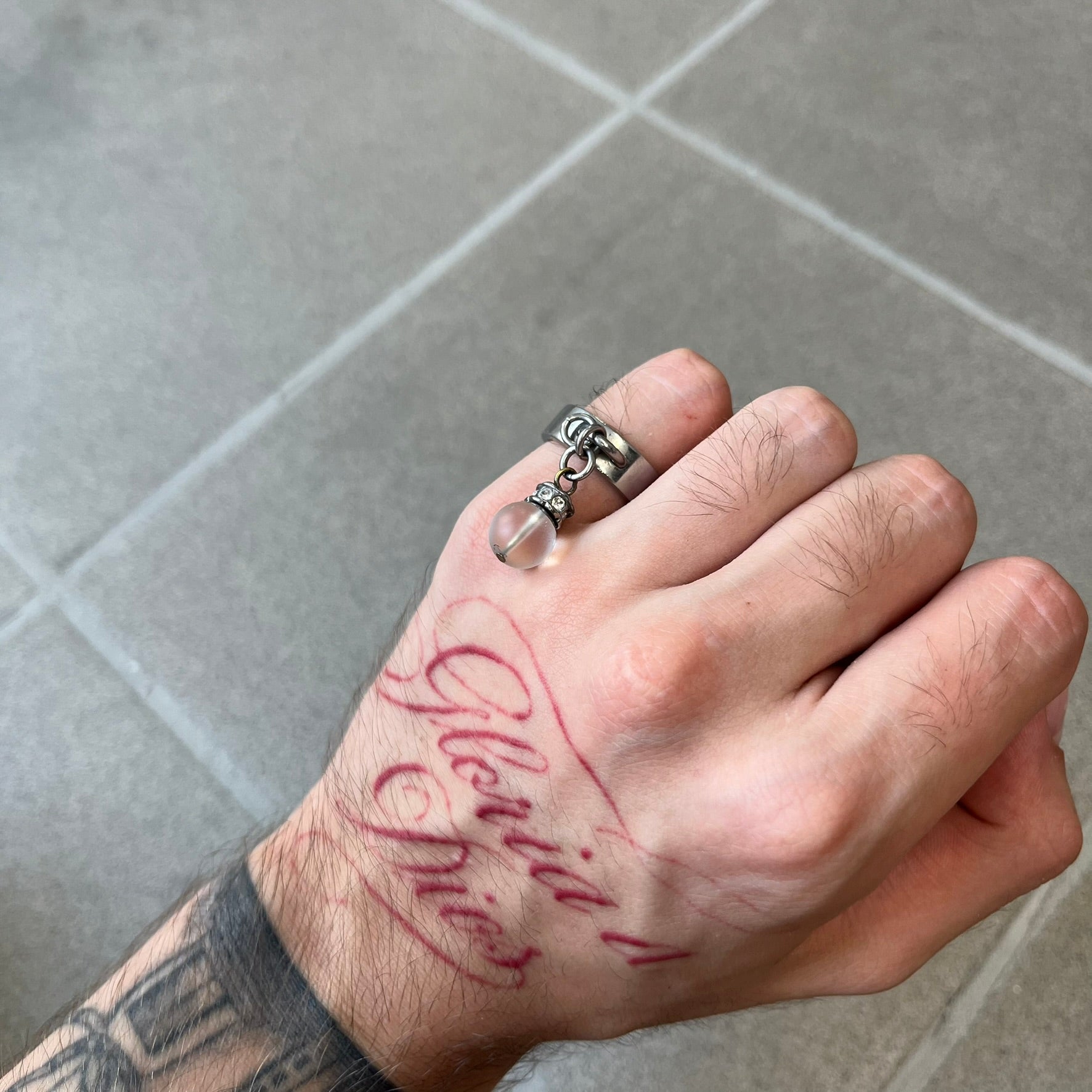 Dolce & Gabbana DJ0305 Pearl Charm Ring features a metal ring with a hanging charm consisting of a pearl with a crystal-like element above it. The charm is loose and moves freely from the ring. One additional charm is missing. The inside of the ring is engraved with a D&G logo.
