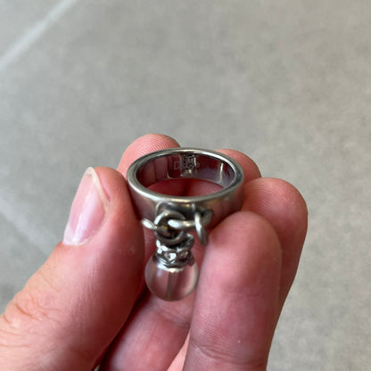 Dolce & Gabbana DJ0305 Pearl Charm Ring features a metal ring with a hanging charm consisting of a pearl with a crystal-like element above it. The charm is loose and moves freely from the ring. One additional charm is missing. The inside of the ring is engraved with a D&G logo.
