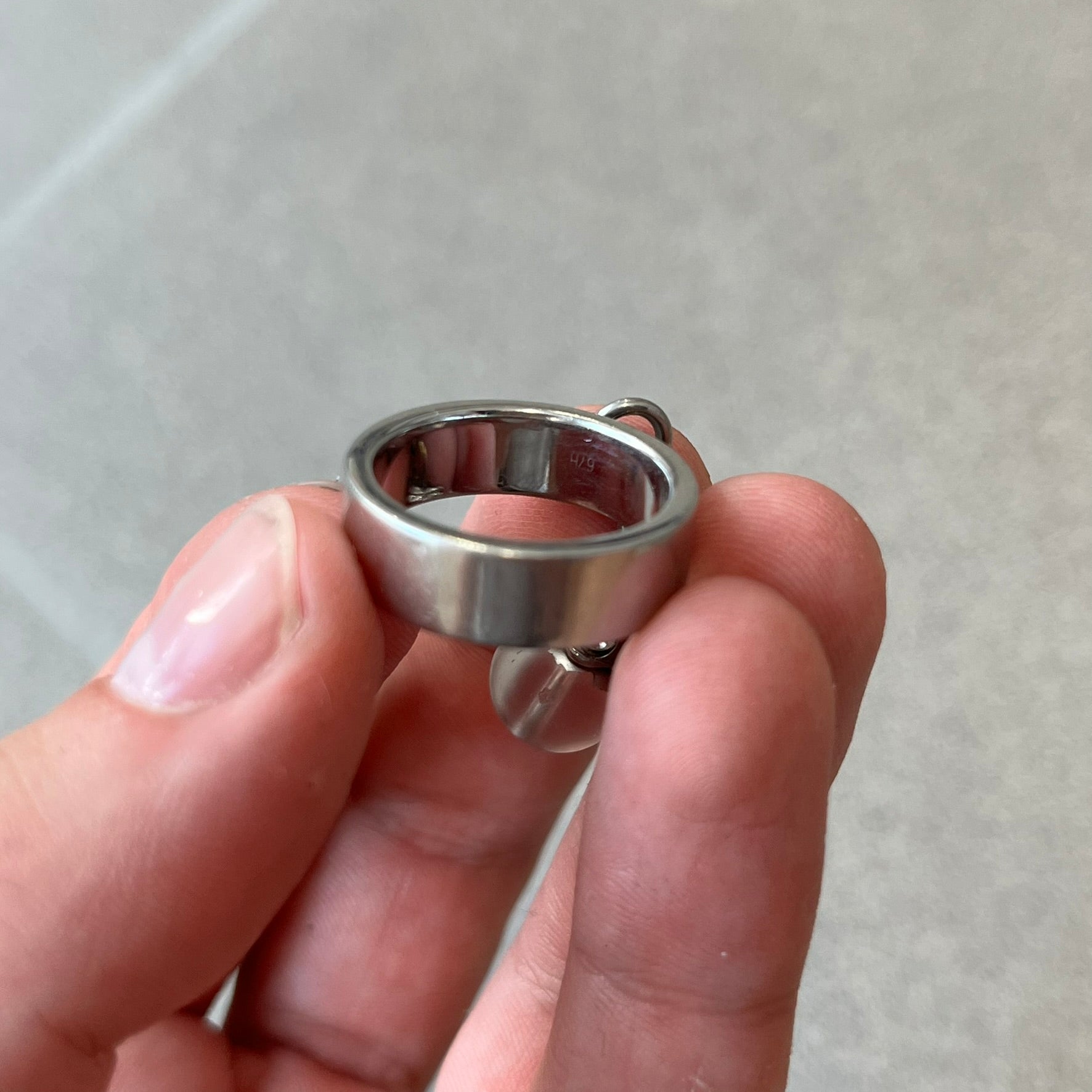 Dolce & Gabbana DJ0305 Pearl Charm Ring features a metal ring with a hanging charm consisting of a pearl with a crystal-like element above it. The charm is loose and moves freely from the ring. One additional charm is missing. The inside of the ring is engraved with a D&G logo.
