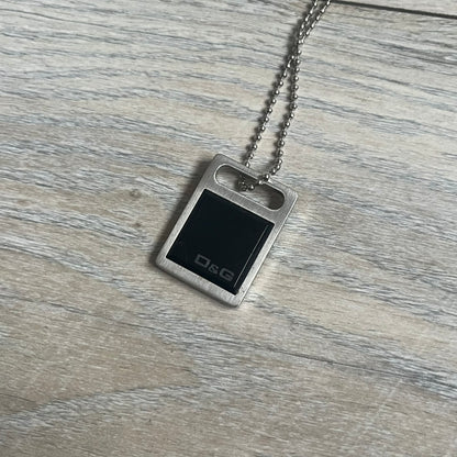 Dolce & Gabbana DJ0430 Black Stone Necklace is a 2000s necklace featuring a stainless steel pendant with a square black stone insert on the front. The lower right corner of the stone is engraved with a D&G logo. It comes with a steel ball chain.