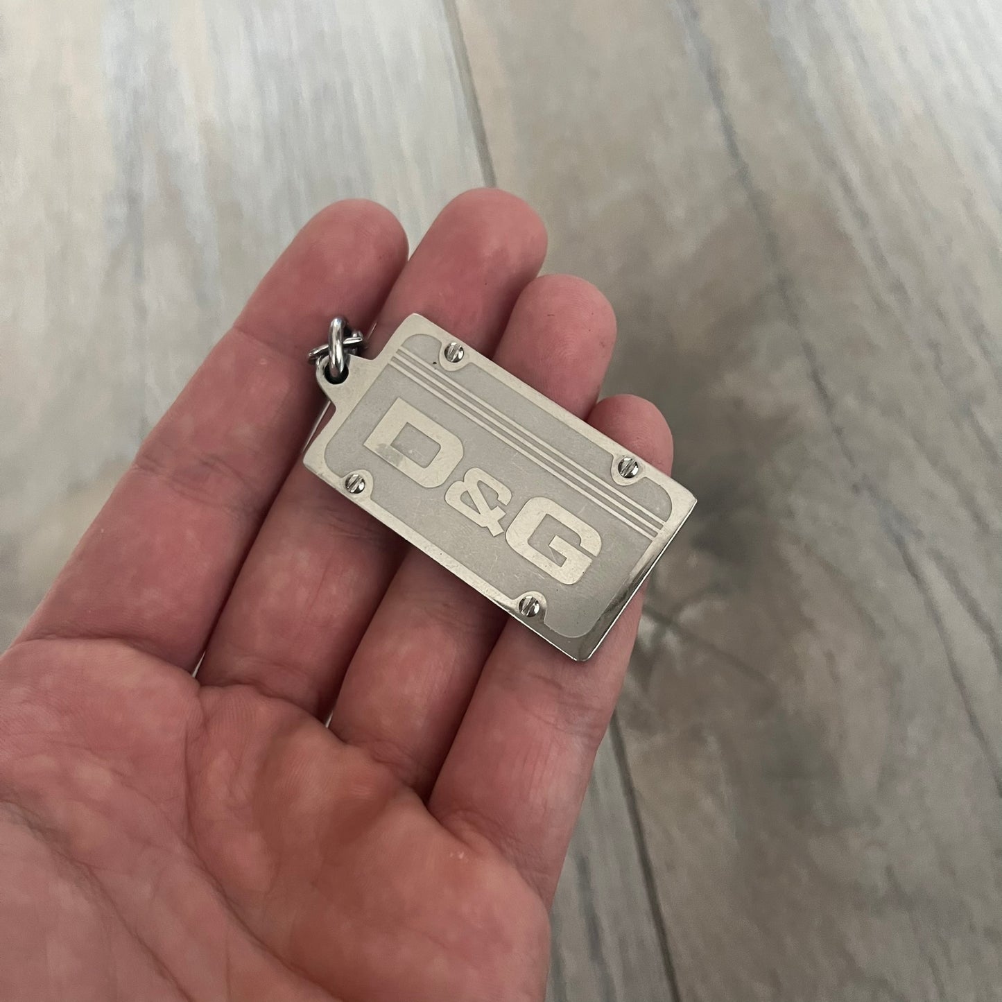 Dolce &amp; Gabbana Propaganda Dog Tag Necklace, featuring a silver stainless steel square tag with four visible screws and the D&amp;G logo engraved on the front. The tag hangs from a durable cable chain, combining sturdy construction with clean, industrial-inspired detailing.