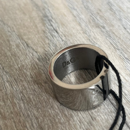 Dolce & Gabbana DJ0551 3 Lines Ring is a stainless steel ring featuring an engraved D&G logo placed vertically along the band. Next to the logo are three parallel lines in black, grey, and white. The design is minimal with a smooth metal finish.