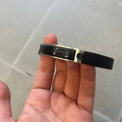 Dolce & Gabbana DJ0574 Black Stone Bracelet is a black leather bracelet featuring a stainless steel central plaque. The plaque includes a rectangular black stone detail with an engraved D&G logo on the right side. The clasp is also engraved with the D&G logo, completing the minimal design.
