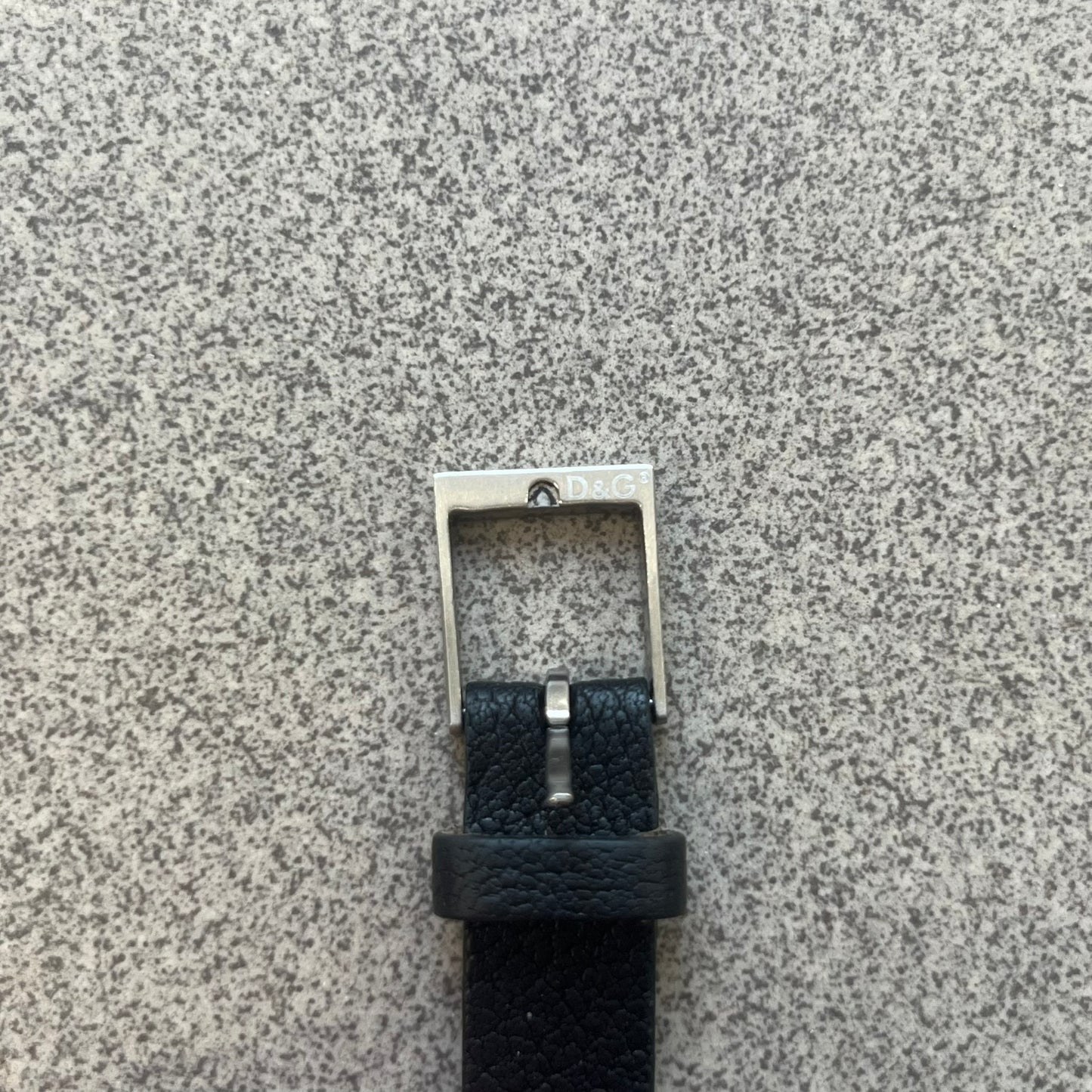 Dolce & Gabbana DJ0574 Black Stone Bracelet is a black leather bracelet featuring a stainless steel central plaque. The plaque includes a rectangular black stone detail with an engraved D&G logo on the right side. The clasp is also engraved with the D&G logo, completing the minimal design.
