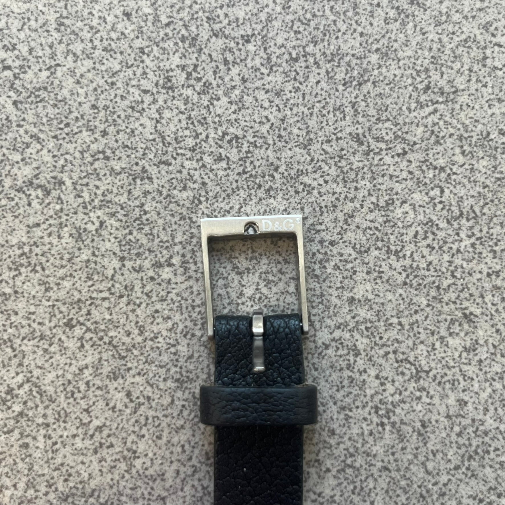 Dolce & Gabbana DJ0574 Black Stone Bracelet is a black leather bracelet featuring a stainless steel central plaque. The plaque includes a rectangular black stone detail with an engraved D&G logo on the right side. The clasp is also engraved with the D&G logo, completing the minimal design.
