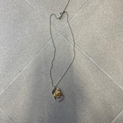Dolce & Gabbana DJ0637 Gold Heart Necklace features a silver-tone stainless steel ball chain with a dog tag-style pendant. The pendant is engraved with a subtle "I" above a gold-tone heart secured by three visible screws, with "D&G" engraved below to form the "I ❤️ D&G" design. The back of the pendant has a "K.O" engraving from a previous owner. Comes with the original dust bag.
