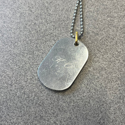 Dolce & Gabbana DJ0637 Gold Heart Necklace features a silver-tone stainless steel ball chain with a dog tag-style pendant. The pendant is engraved with a subtle "I" above a gold-tone heart secured by three visible screws, with "D&G" engraved below to form the "I ❤️ D&G" design. The back of the pendant has a "K.O" engraving from a previous owner. Comes with the original dust bag.
