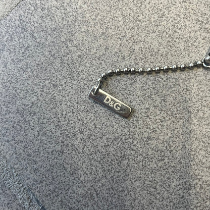 Dolce & Gabbana DJ0637 Gold Heart Necklace features a silver-tone stainless steel ball chain with a dog tag-style pendant. The pendant is engraved with a subtle "I" above a gold-tone heart secured by three visible screws, with "D&G" engraved below to form the "I ❤️ D&G" design. The back of the pendant has a "K.O" engraving from a previous owner. Comes with the original dust bag.
