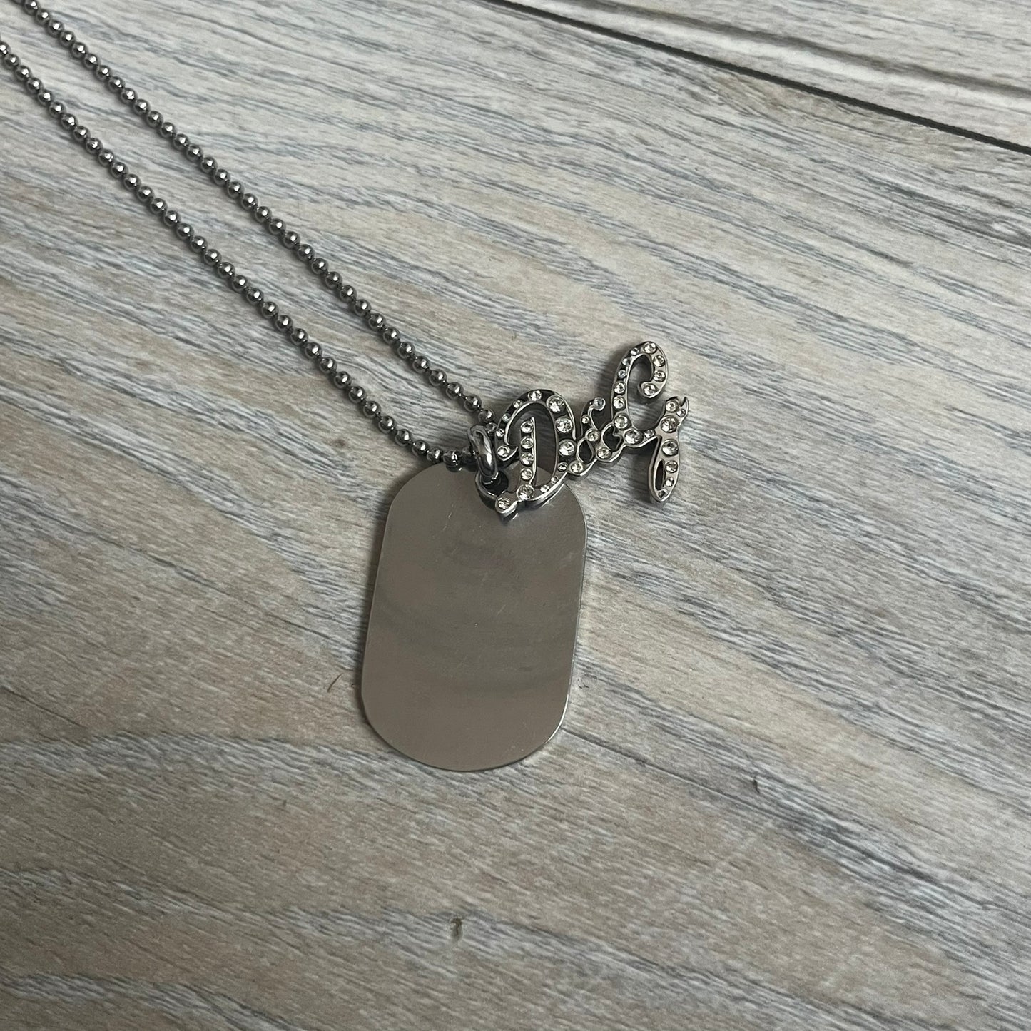 The Dolce &amp; Gabbana Crystal Logo Dog Tag Necklace features a silver-tone ball chain with two pendants: a plain dog tag and a cutout D&amp;G logo adorned with crystals. It has a large clasp engraved with D&amp;G and model markings, from the 2000s.