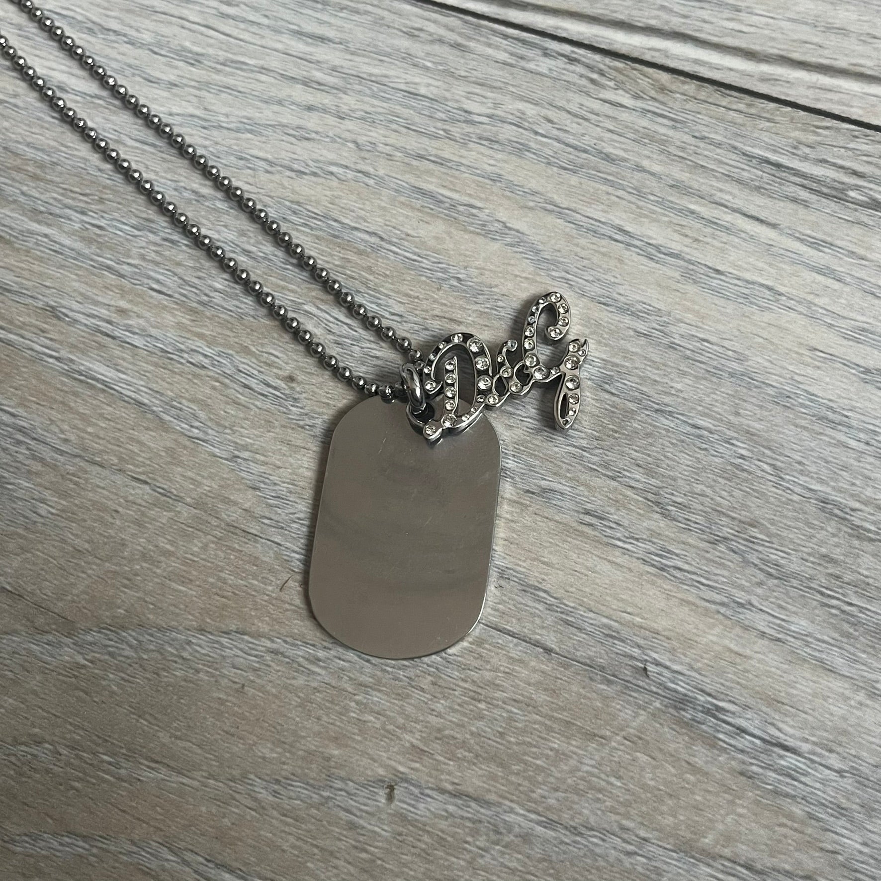 The Dolce &amp; Gabbana Crystal Logo Dog Tag Necklace features a silver-tone ball chain with two pendants: a plain dog tag and a cutout D&amp;G logo adorned with crystals. It has a large clasp engraved with D&amp;G and model markings, from the 2000s.