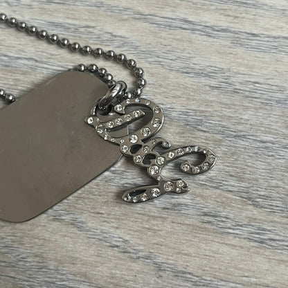 The Dolce &amp; Gabbana Crystal Logo Dog Tag Necklace features a silver-tone ball chain with two pendants: a plain dog tag and a cutout D&amp;G logo adorned with crystals. It has a large clasp engraved with D&amp;G and model markings, from the 2000s.