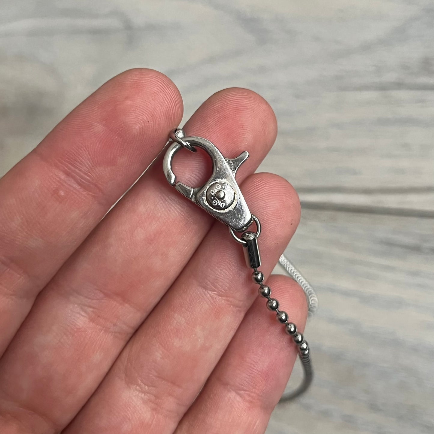 The Dolce &amp; Gabbana Crystal Logo Dog Tag Necklace features a silver-tone ball chain with two pendants: a plain dog tag and a cutout D&amp;G logo adorned with crystals. It has a large clasp engraved with D&amp;G and model markings, from the 2000s.