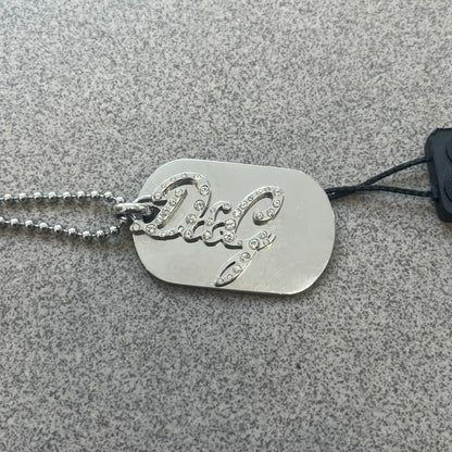 The Dolce &amp; Gabbana Crystal Logo Dog Tag Necklace features a silver-tone ball chain with two pendants: a plain dog tag and a cutout D&amp;G logo adorned with crystals. It has a large clasp engraved with D&amp;G and model markings, from the 2000s.