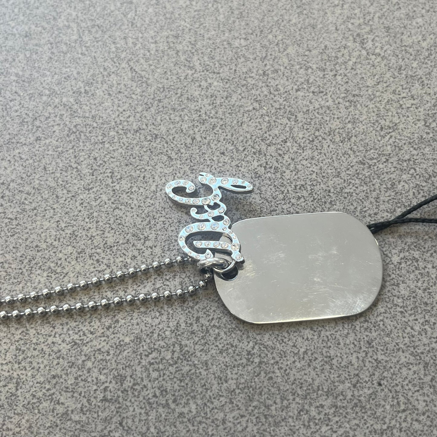 The Dolce &amp; Gabbana Crystal Logo Dog Tag Necklace features a silver-tone ball chain with two pendants: a plain dog tag and a cutout D&amp;G logo adorned with crystals. It has a large clasp engraved with D&amp;G and model markings, from the 2000s.