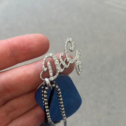 The Dolce &amp; Gabbana Crystal Logo Dog Tag Necklace features a silver-tone ball chain with two pendants: a plain dog tag and a cutout D&amp;G logo adorned with crystals. It has a large clasp engraved with D&amp;G and model markings, from the 2000s.