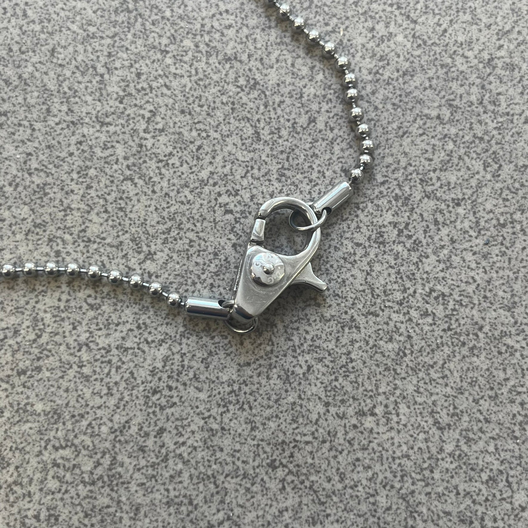 The Dolce &amp; Gabbana Crystal Logo Dog Tag Necklace features a silver-tone ball chain with two pendants: a plain dog tag and a cutout D&amp;G logo adorned with crystals. It has a large clasp engraved with D&amp;G and model markings, from the 2000s.