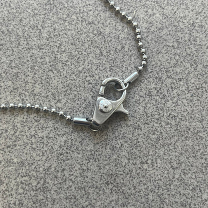 The Dolce &amp; Gabbana Crystal Logo Dog Tag Necklace features a silver-tone ball chain with two pendants: a plain dog tag and a cutout D&amp;G logo adorned with crystals. It has a large clasp engraved with D&amp;G and model markings, from the 2000s.