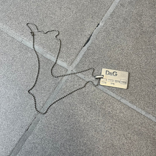 Dolce &amp; Gabbana 2000s Credit Card Necklace (DJ0772) is a rare stainless steel necklace featuring a credit card-shaped pendant. The pendant includes a large raised D&amp;G logo, an engraved D&amp;G logo, and embossed numbers inspired by a real credit card. The chain is not D&amp;G - it's a basic steel ball chain, only the pendant is from Dolce.