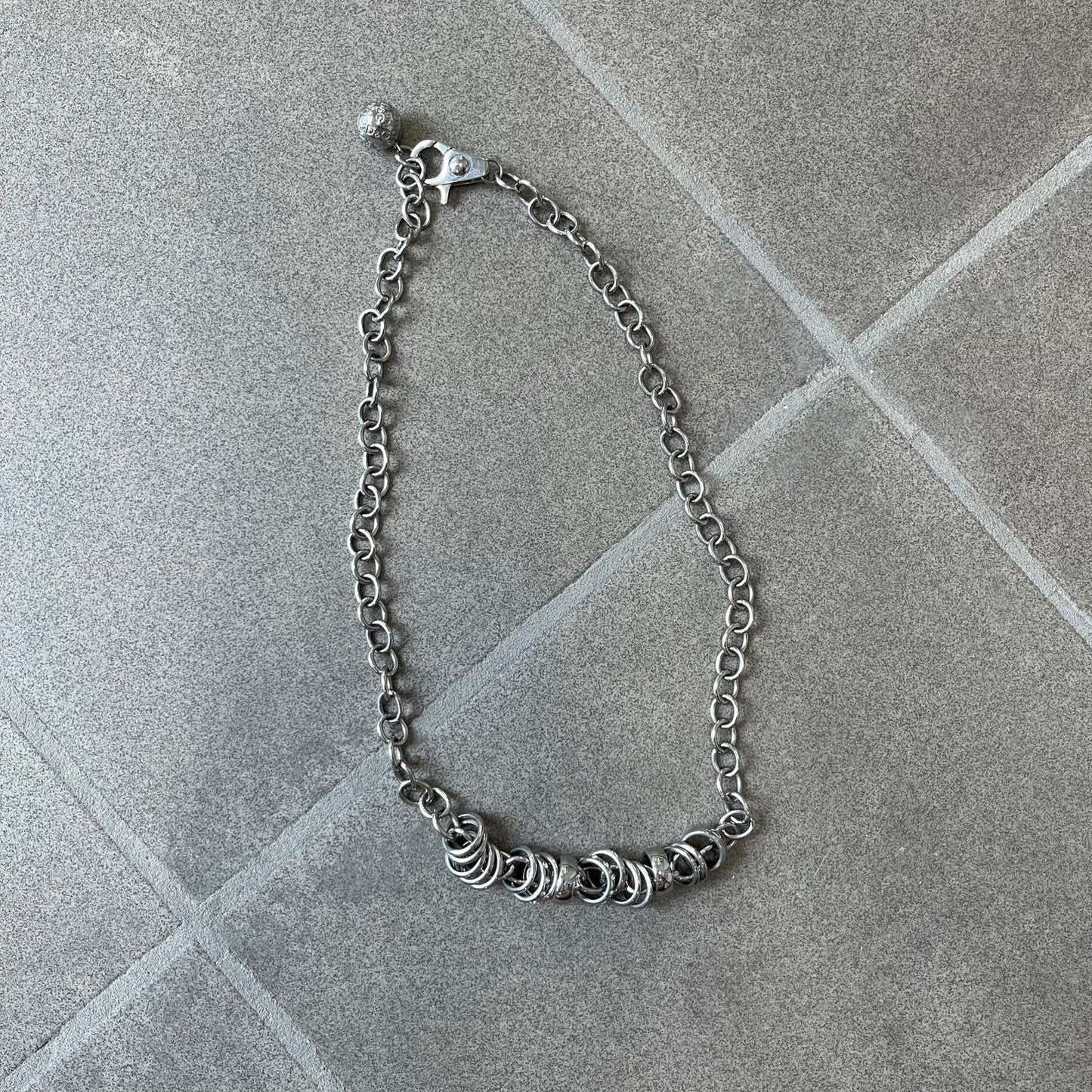 Dolce &amp; Gabbana DJ0776 Crystal Ring Link Necklace features a long stainless steel chain with freely moving rings, including basic loops, D&amp;G-engraved rings and crystal-set rings. The necklace has a large clasp, while the end is finished with a ball featuring D&amp;G logos all around it.