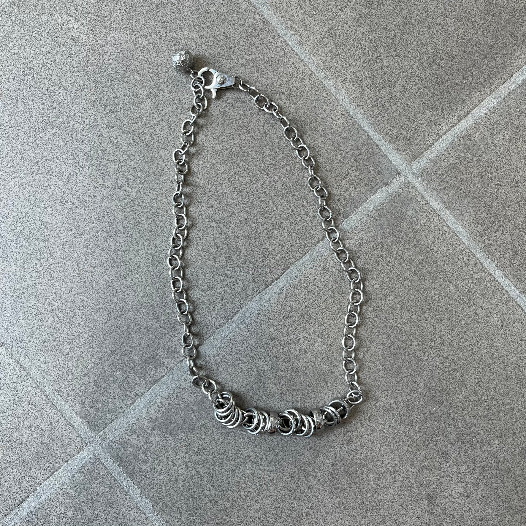 Dolce &amp; Gabbana DJ0776 Crystal Ring Link Necklace features a long stainless steel chain with freely moving rings, including basic loops, D&amp;G-engraved rings and crystal-set rings. The necklace has a large clasp, while the end is finished with a ball featuring D&amp;G logos all around it.