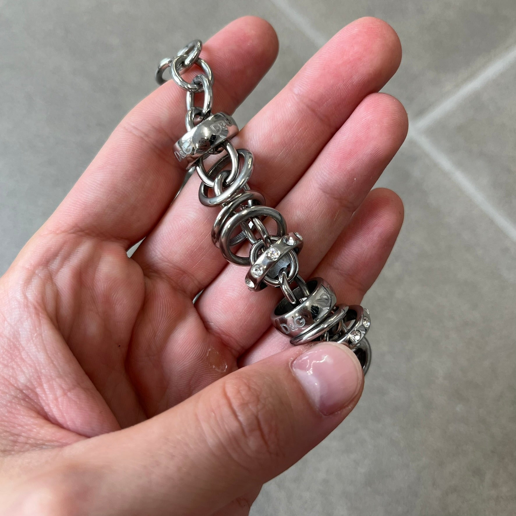 Dolce &amp; Gabbana DJ0776 Crystal Ring Link Necklace features a long stainless steel chain with freely moving rings, including basic loops, D&amp;G-engraved rings and crystal-set rings. The necklace has a large clasp, while the end is finished with a ball featuring D&amp;G logos all around it.