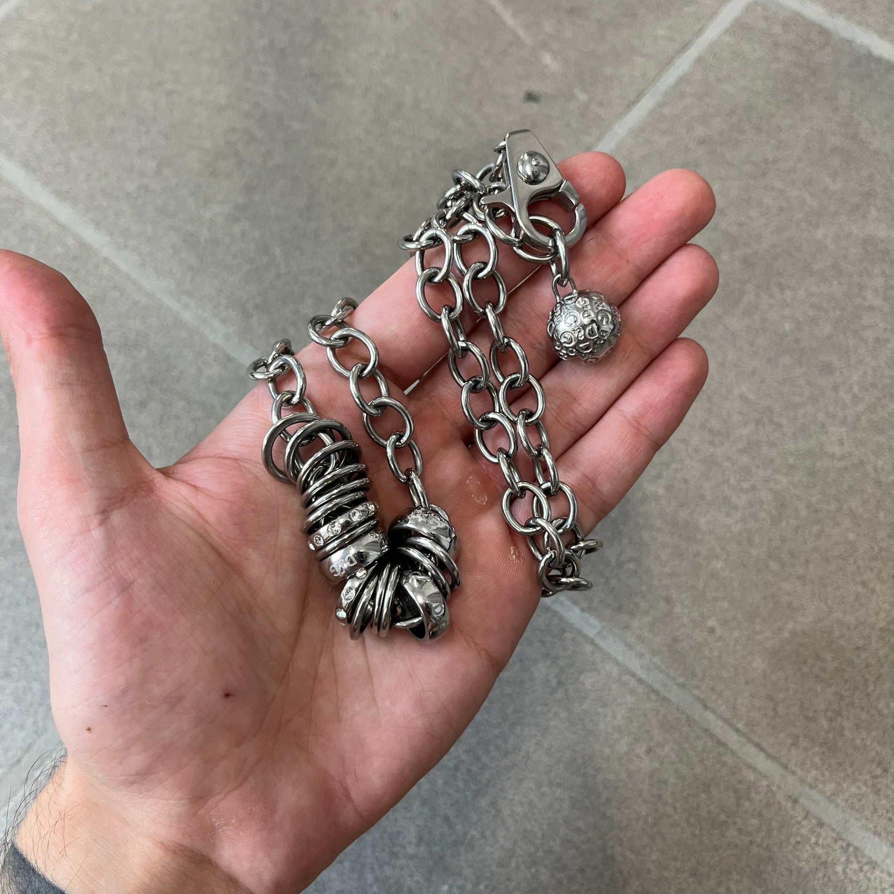 Dolce &amp; Gabbana DJ0776 Crystal Ring Link Necklace features a long stainless steel chain with freely moving rings, including basic loops, D&amp;G-engraved rings and crystal-set rings. The necklace has a large clasp, while the end is finished with a ball featuring D&amp;G logos all around it.