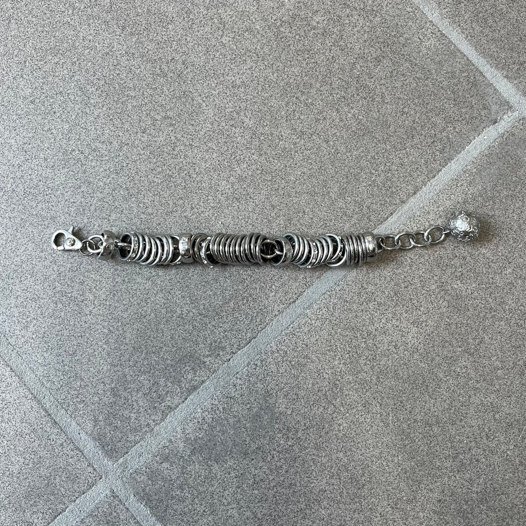 Dolce &amp; Gabbana DJ0777 Crystal Ring Link Bracelet features a stainless steel chain with freely moving rings, including basic loops, D&amp;G-engraved rings and crystal-set rings. The bracelet has a large clasp, while the end is finished with a ball featuring D&amp;G logos all around it.